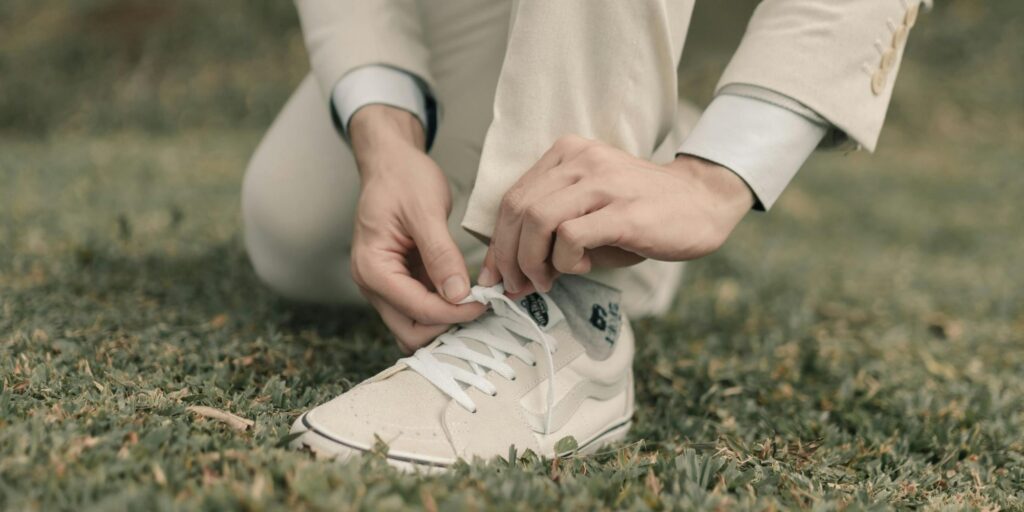 A man tying his shoelaces. He is wearing a beige suit and informal sneakers