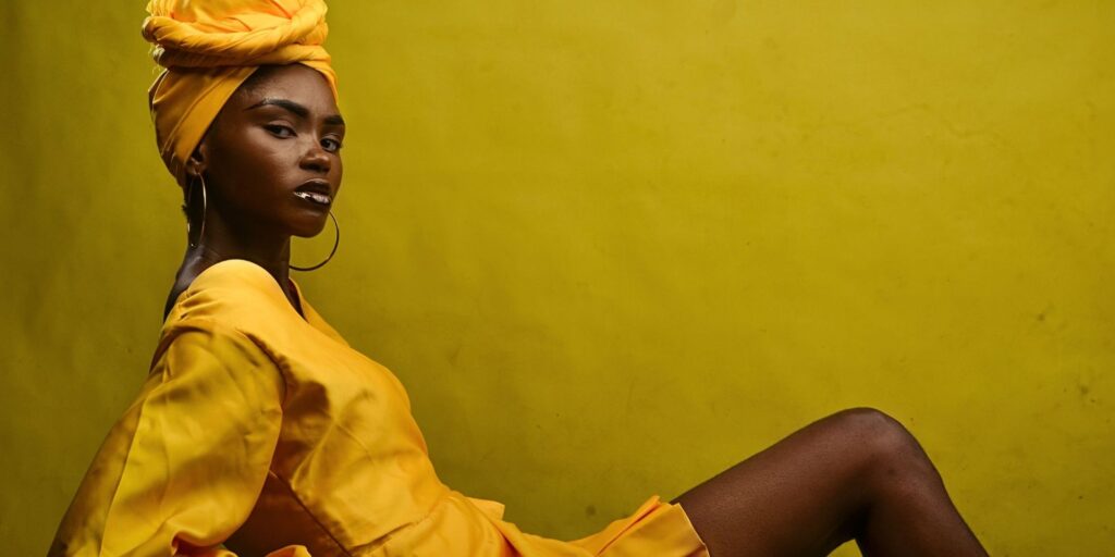Beautiful woman wearing a yellow dress and head scarf, lying down in front of a yellow wall