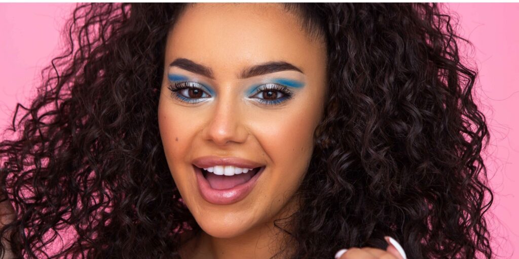 Woman with big curly hair, smiling. She has blue eyeshadow on from Ulta