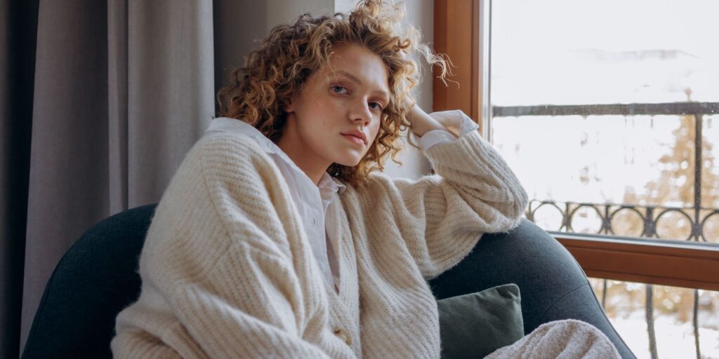A woman with blonde curly hair looking cozy on an armchair