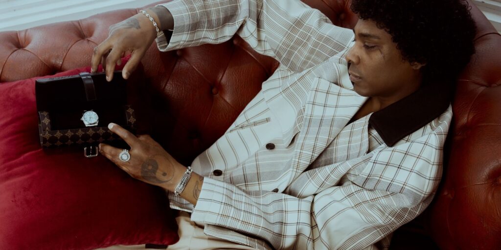 Man reclining on a couch in a nice white suite, holding a man-bag