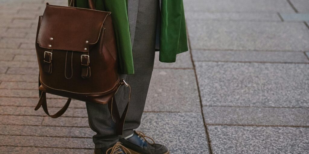 someone holding a leather backpack. She has grey pants and a green jacket