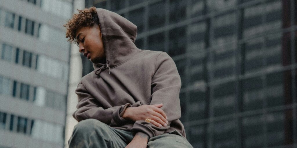 Young man looking over the edge of a building in the city. He is wearing a grey hoodie and jeans