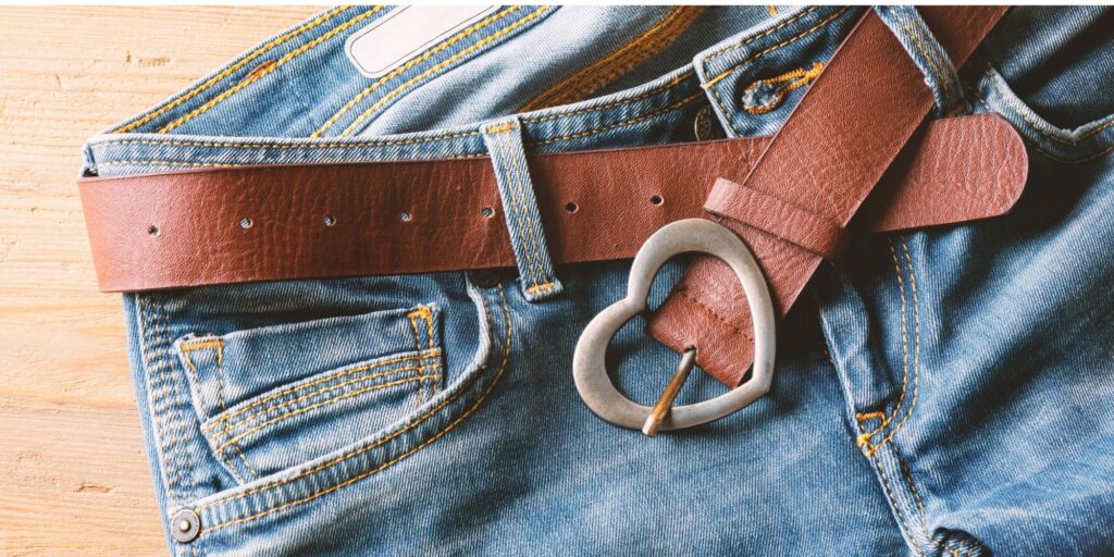 A pair of jeans with a brown leather belt that has a heart-shaped buckle
