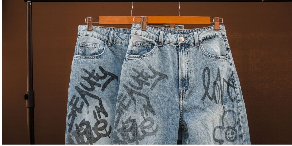 2 pairs of jeans hanging up. They are light coloured with black graffiti on them