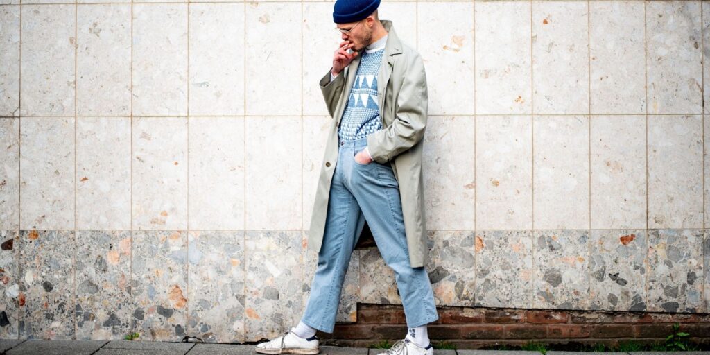 man smoking a cigarette, wearing a light blue outfit with a trench coat over the top