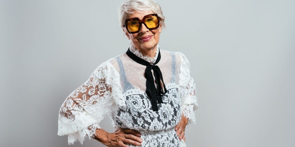 An old lady dressed in younger fashion with large sunglasses and a lace top