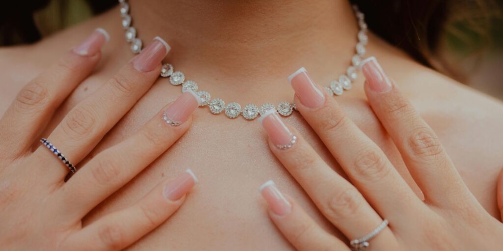 A woman is wearing a diamond necklace and has a beautiful manicure