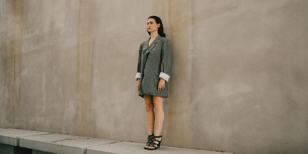 Woman wearing a green oversized blazer standing weirdly with her back against a wall