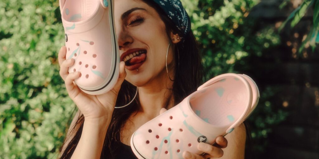 Woman holding pink crocs and poking her tongue out