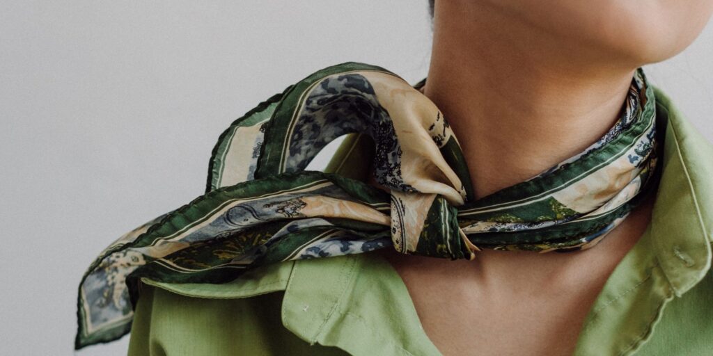 Green silk scarf tied fashionable around a woman's neck as an essential accessories