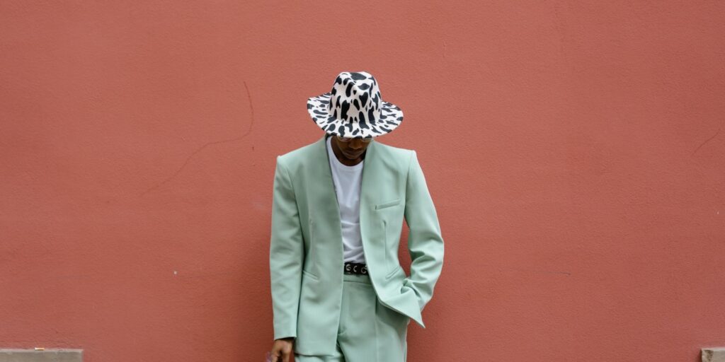 Stylish man leaning against an orange wall wearing a green suite and cow-hide hat. Breaking the fashion rules