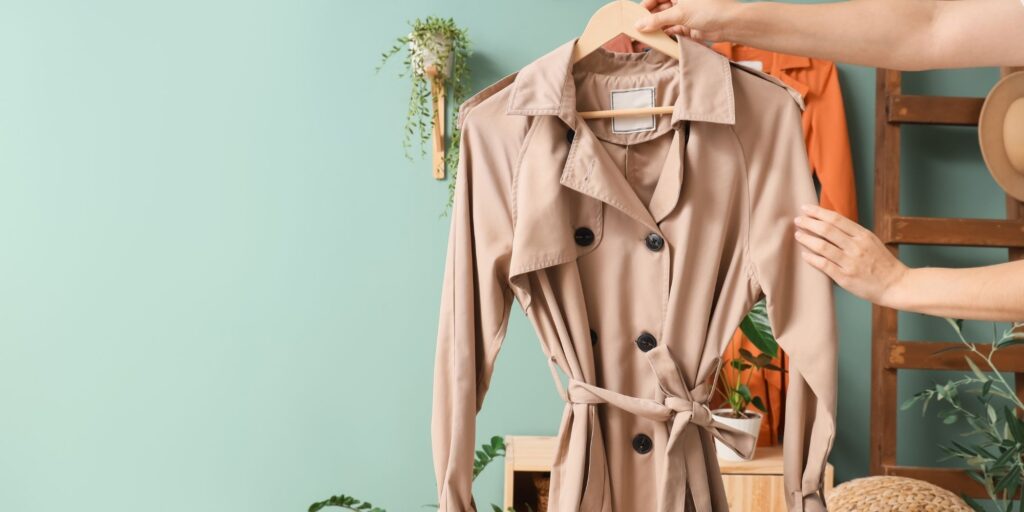 A trench coat being held out on a clothes hanger against a new look green wall.