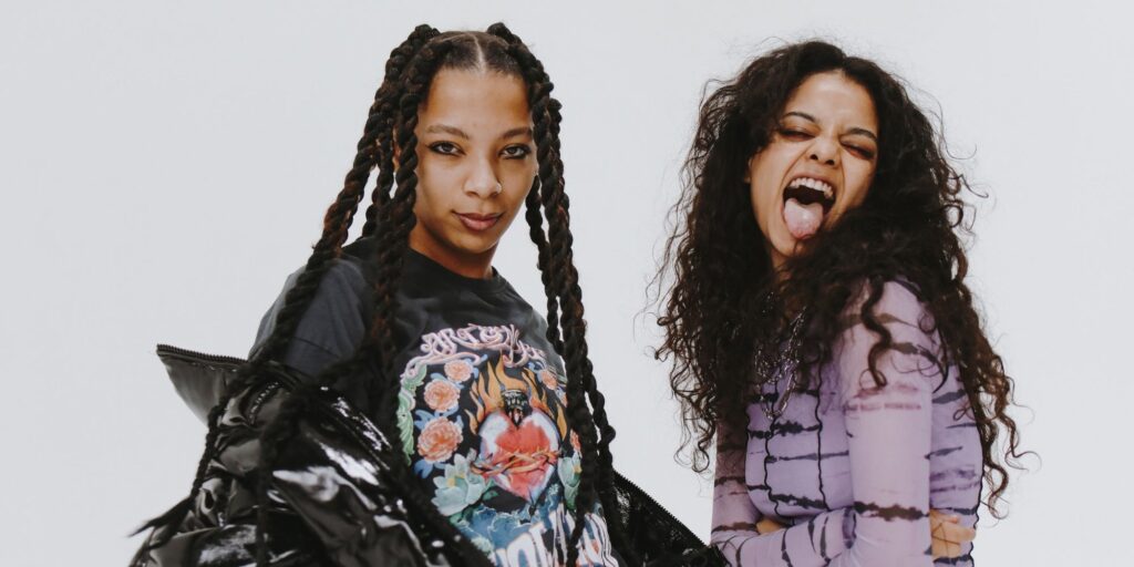 Two young email women posing for the camera. One is sticking out her tongue. The other is wearing a black puffer jacket