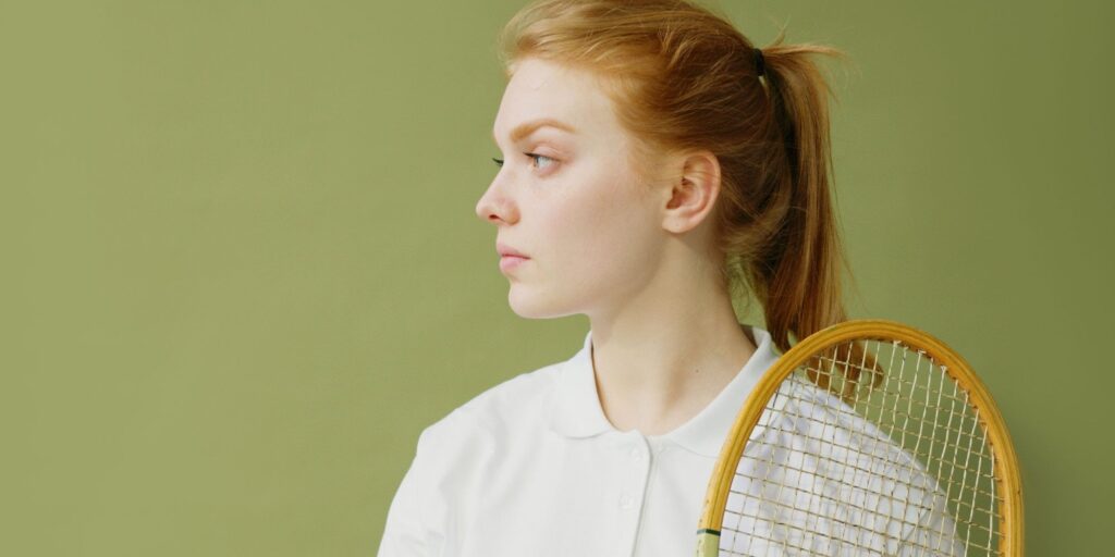 Woman with red hair looking to the left and holding a badminton racket