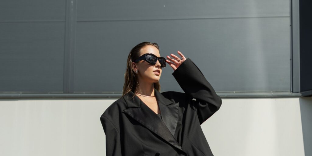 A woman walking in a black blazer and wearing black sunglasses