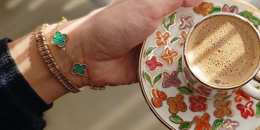 A close up of a wrist wearing a van cleef bracelet holding a cup of coffee