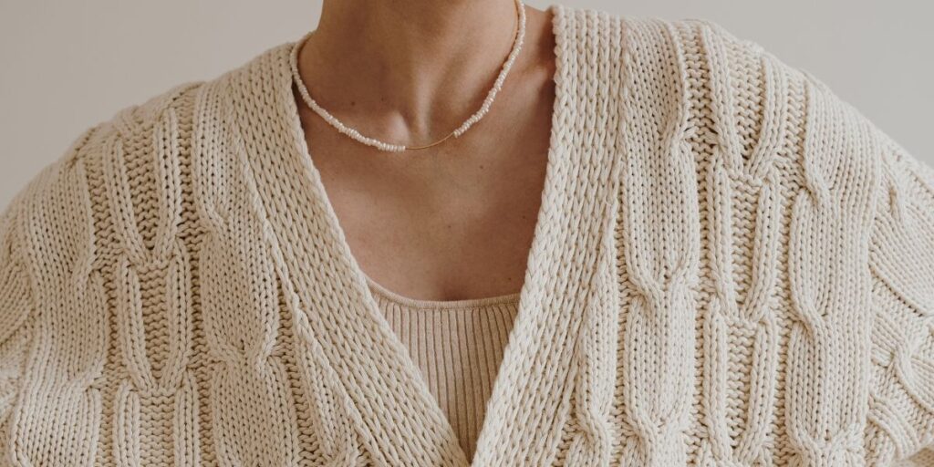 Top half of a woman wearing a cardigan and a simple necklace